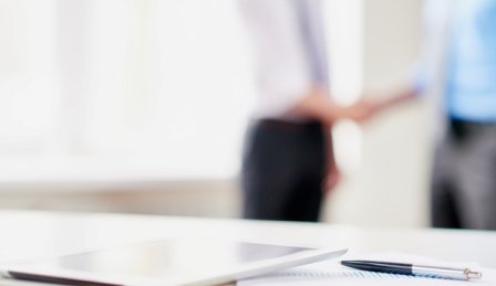 Image of office desk with pen in focus, people in office wear in the background