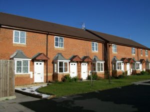 A street of small, cottage-style red brick houses against a blue sky
